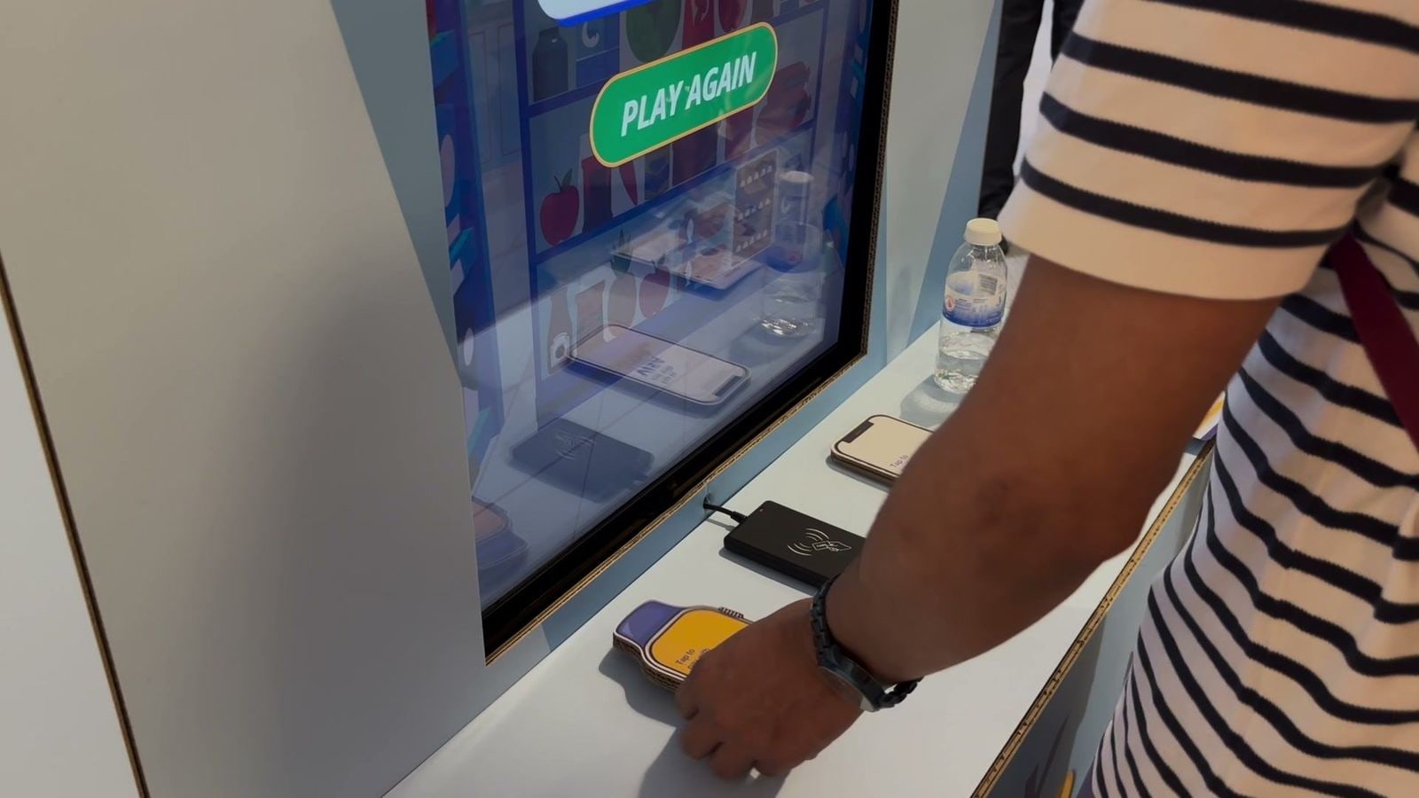 A Visa smartwatch prop tapped on the NFC card reader at the Visa Family Day station, with the qiksense game on screen
