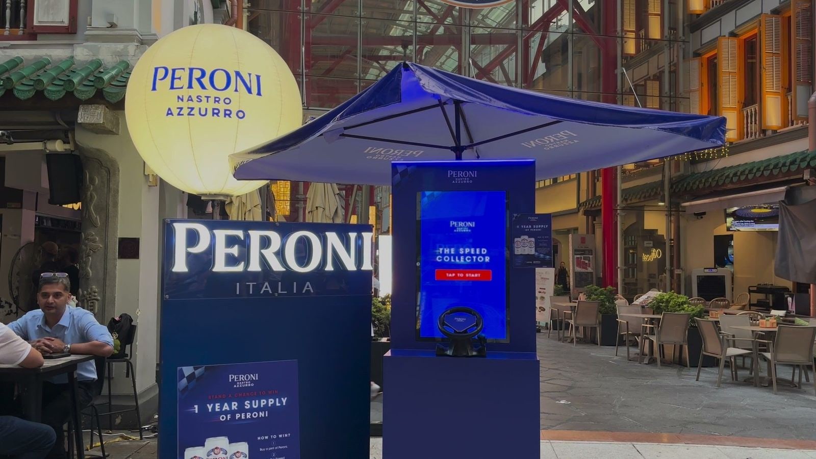 The Peroni booth at Far East Square by day, with the Speed Collector start screen and the racing wheel powered by qiksense