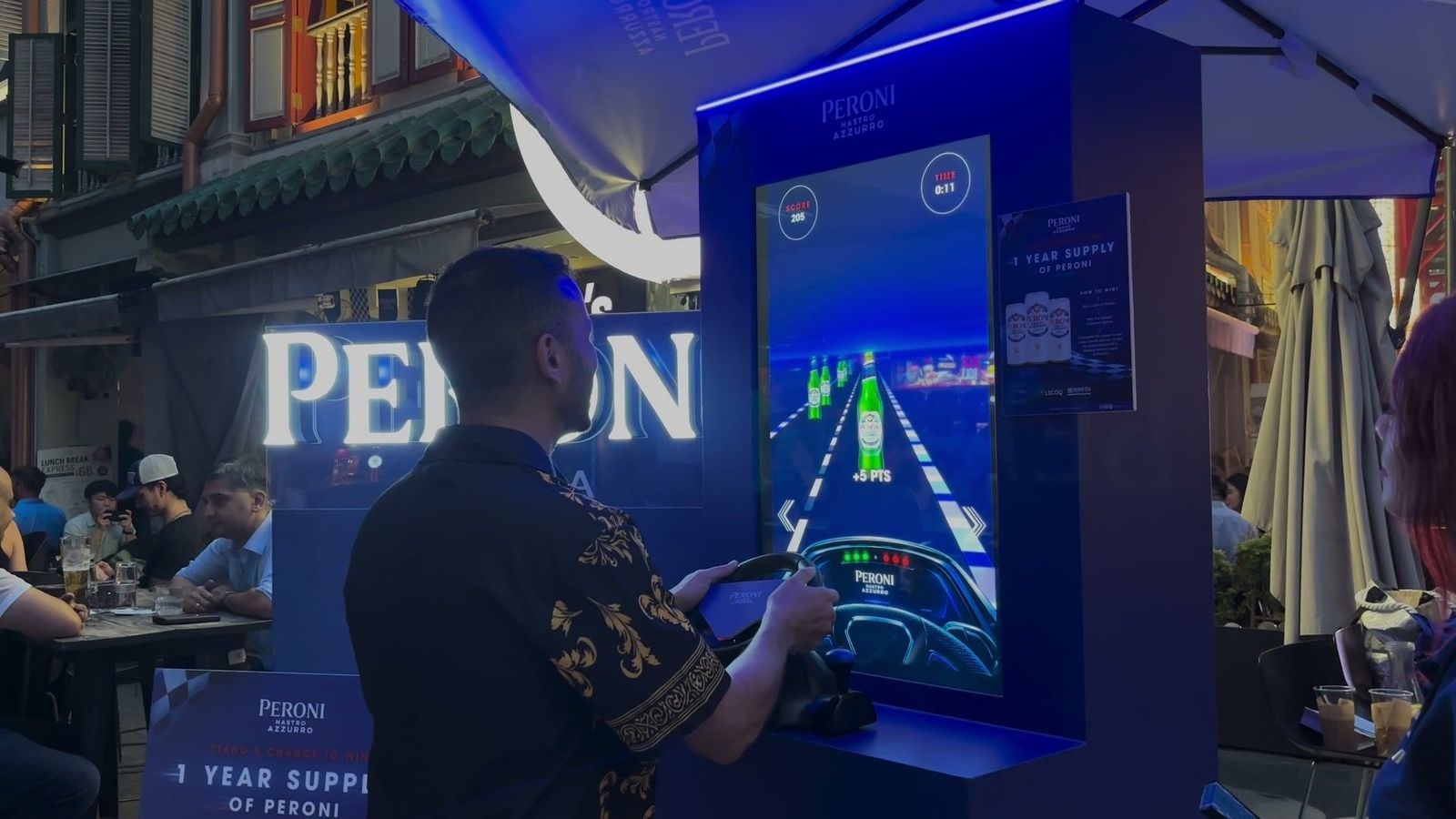 A guest turning the racing wheel in front of the Speed Collector screen at the Peroni booth, with the game run on qiksense